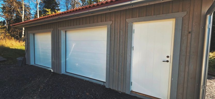 En träbyggnad med två stora vita garageportar och en dörr.
