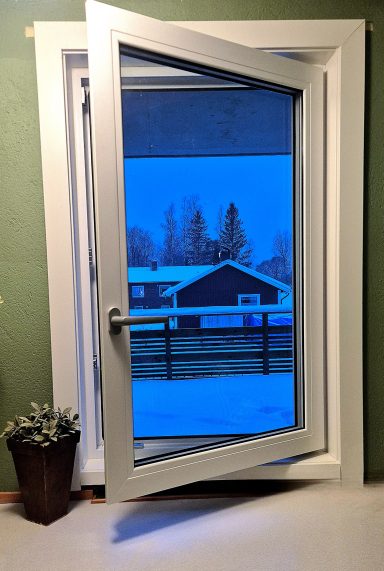 Öppen fönsterdörr med snö och ett hus i bakgrunden. Grön vägg inomhus.