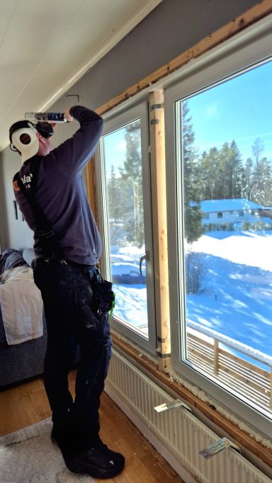 Person installerar fönster i ett rum med snöigt landskap utanför.