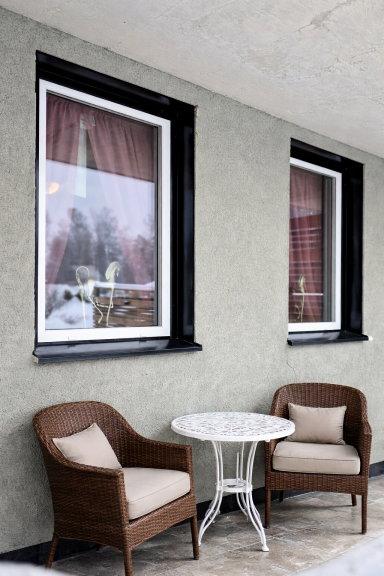 Två brunfärgade stolar och ett litet bord vid fönster med röda gardiner.