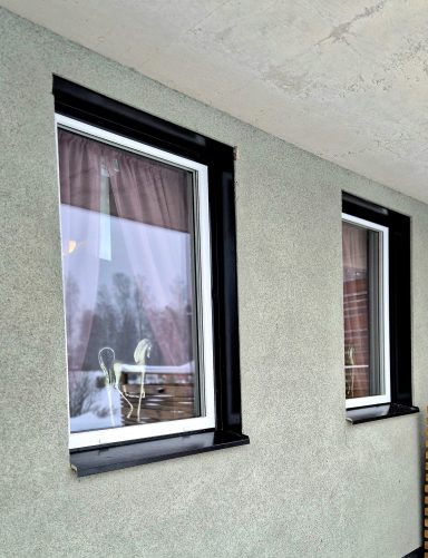 Flera fönster med svarta ramar och röda gardiner på en grå vägg.